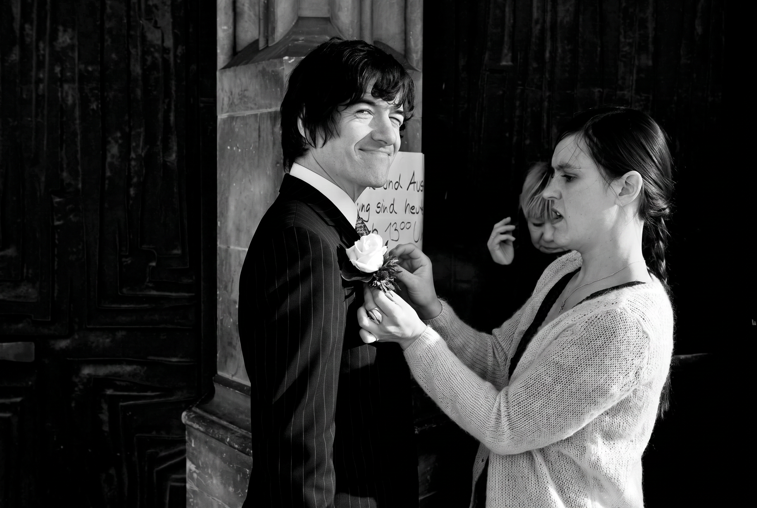 Black and white photograph of a groom having his buttonhole pinned on outside the church